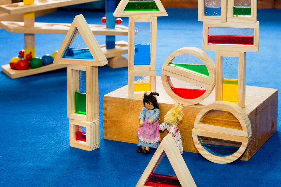 Holzbausteine und 2 kleine Puppen auf einem blauen Teppich